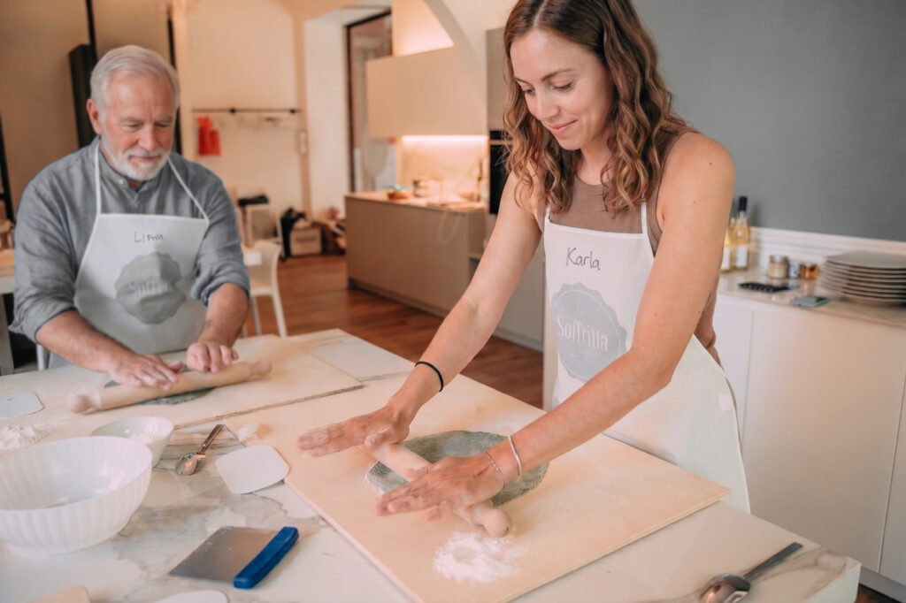 Una ragazza e un signore stendono la pasta fresca durante un cooking class