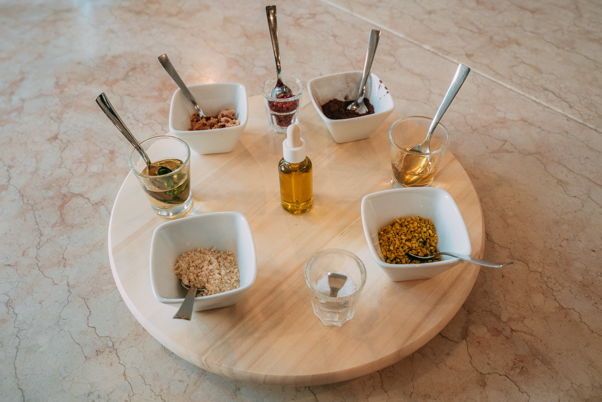Ciotoline con spezie, semi e olio disposte su un vassoio rotondo in legno per la preparazione di una ricetta
