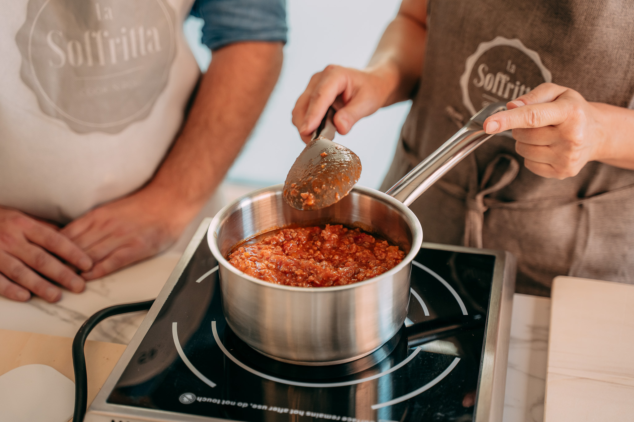 Pentola con sugo di pomodoro e carne su un fornello a induzione durante la preparazione del ragù