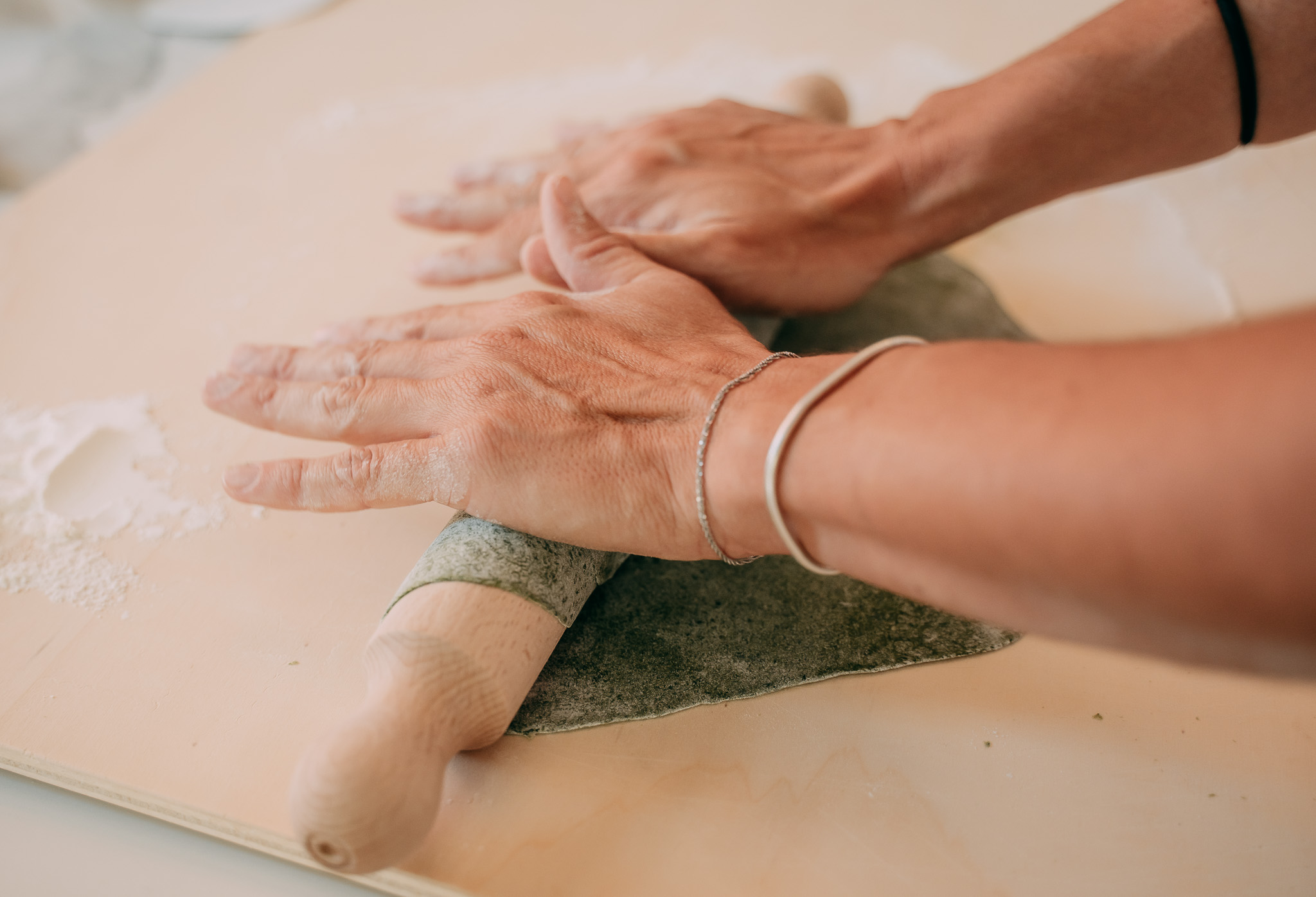 Mani che stendono l'impasto della pasta fresca con un mattarello