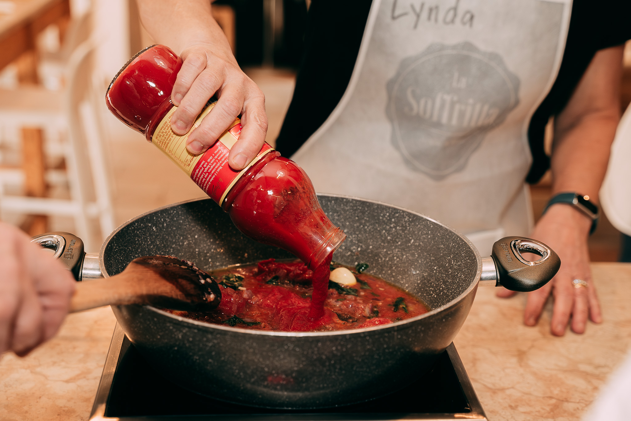 Mano che aggiunge salsa di pomodoro in padella durante la preparazione del sugo