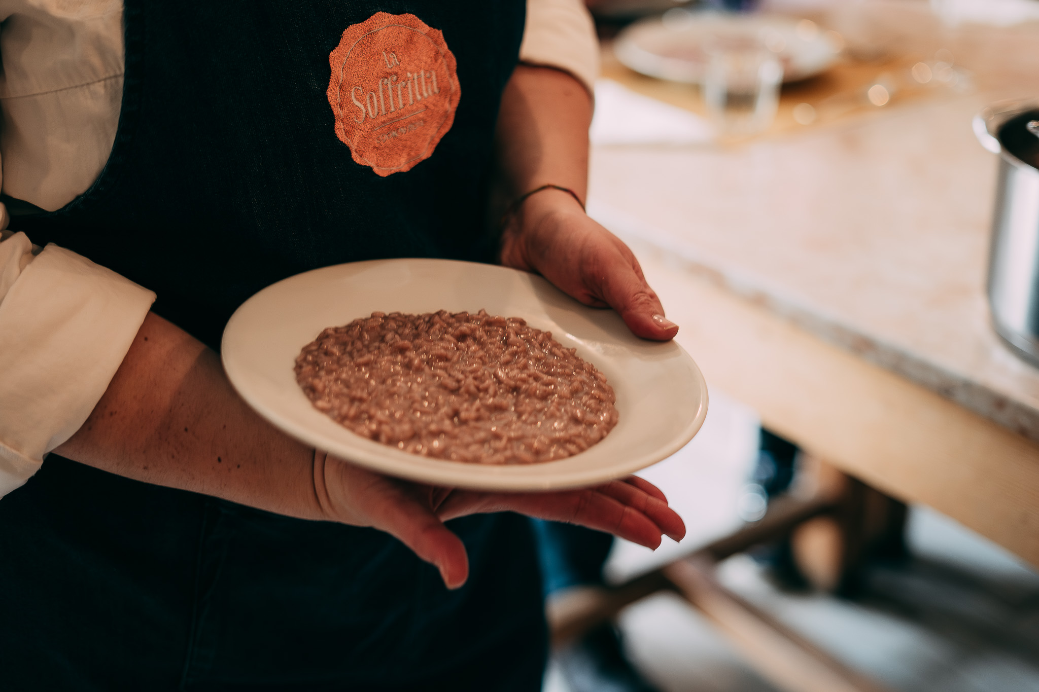 Mani che reggono un piatto di risotto all'Amarone preparato durante una class de La Soffritta