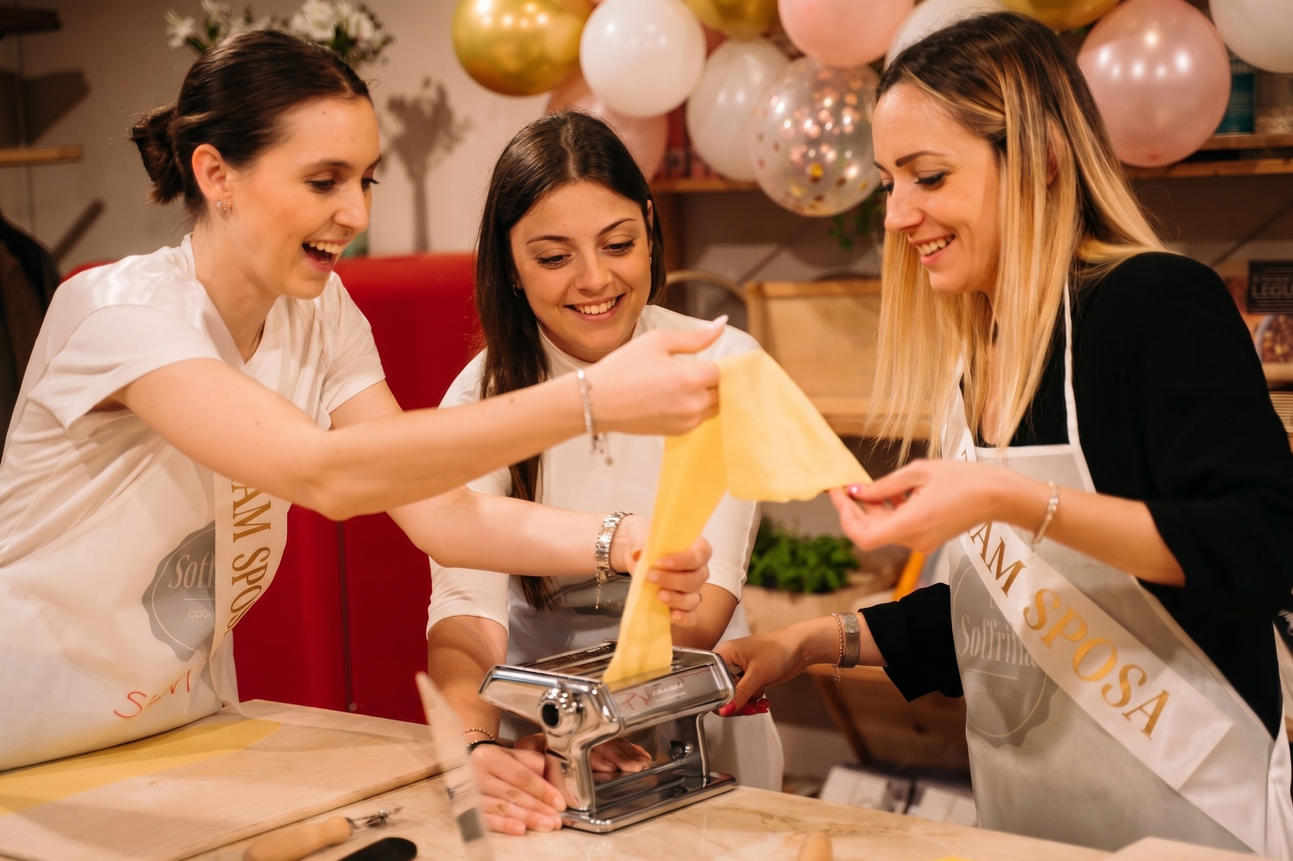 Tre ragazze stendono insieme la pasta con la macchina per la pasta fresca
