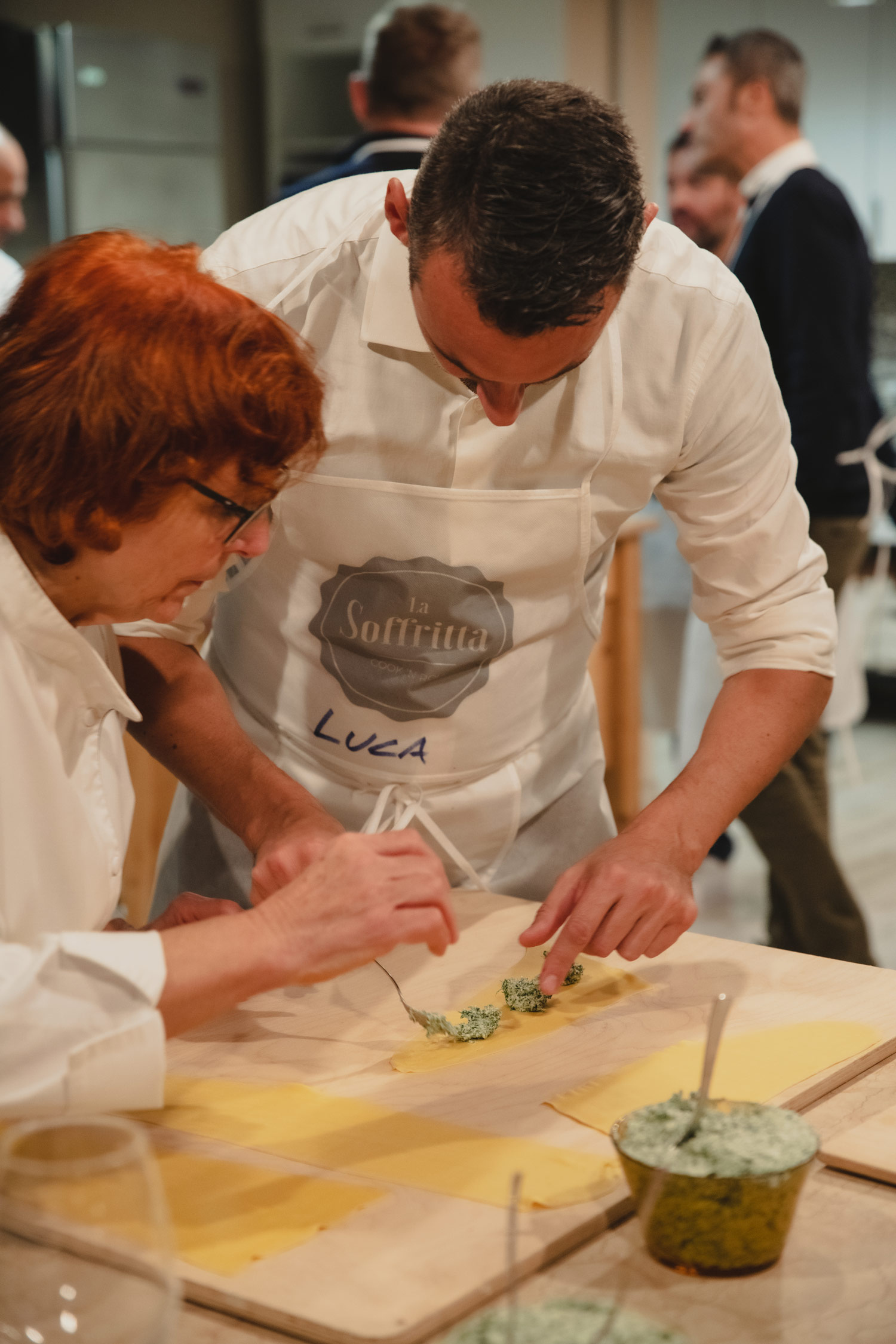 Cuoca aiuta un partecipante del Team Cooking a farcire la pasta fresca