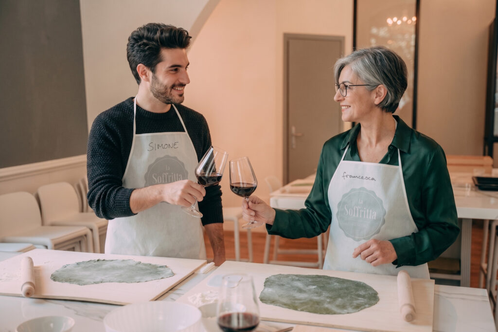 Un ragazzo e una signora brindano con vino bianco durante una lezione di cucina