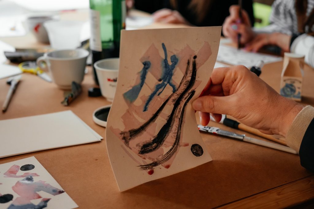 Hand holding a sheet of paper painted with abstract black ink strokes and color gradients, during an art workshop