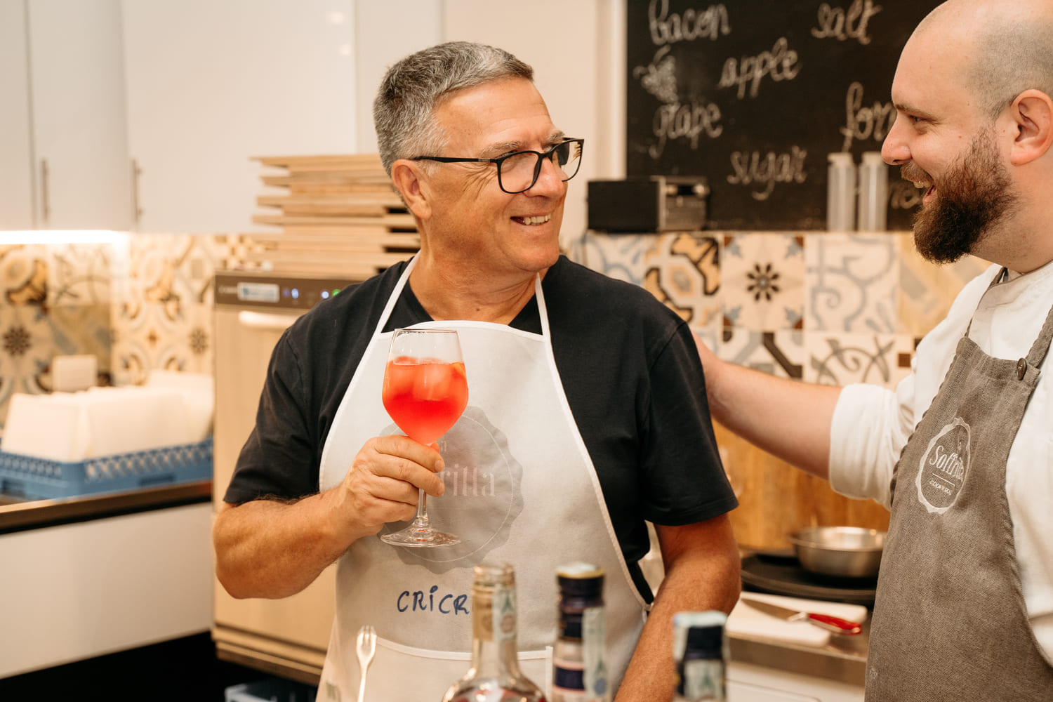 A participant holding an Aperol Spritz looks and smiles at the chef