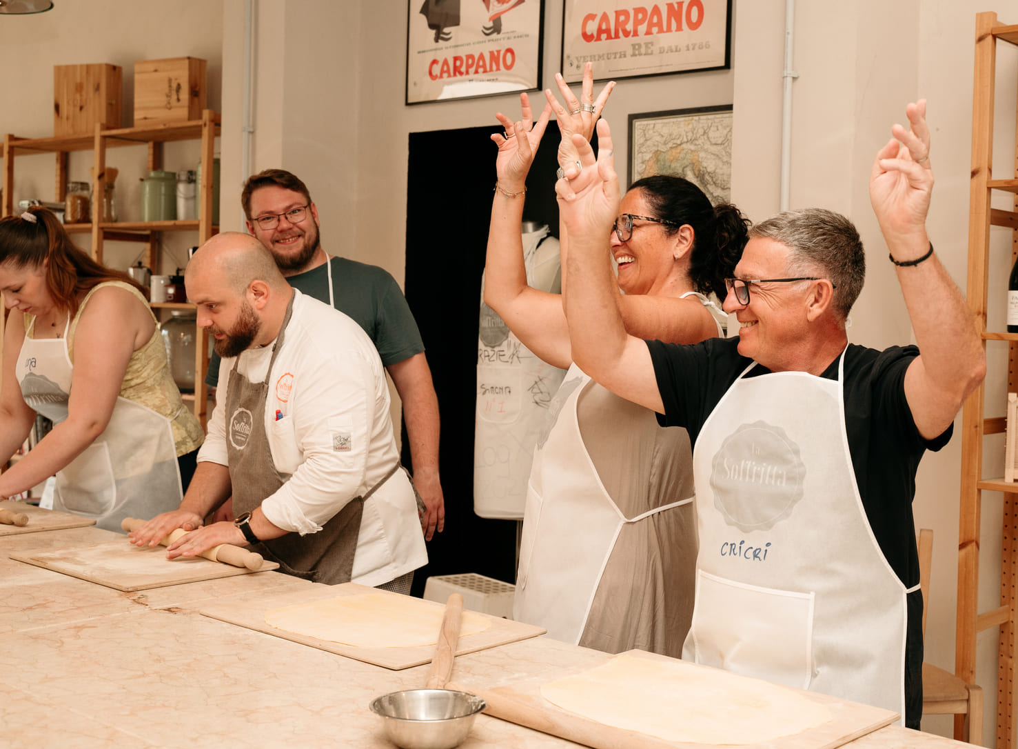 Group of people in a cooking school kneading pasta dough with wooden rolling pins on a long table