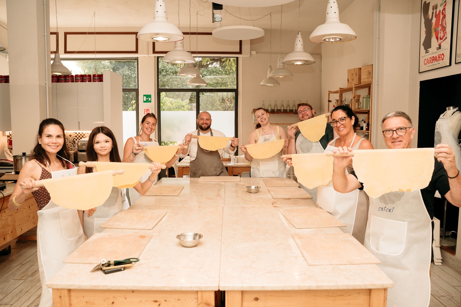Group photo of participants the kitchen holding up their handmade pasta dough