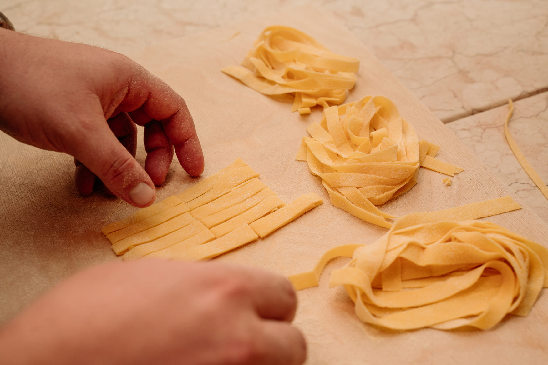 Close-up of a person's hands shaping and placing fresh pasta nests onto a flour-dusted surface