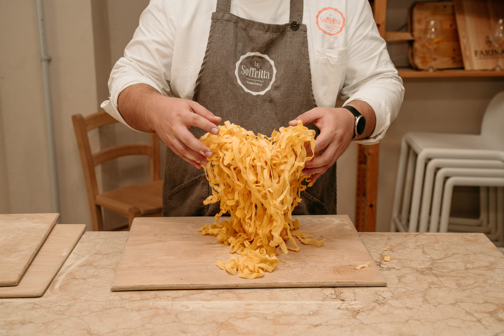 Close-up view of a chef's hands presenting a large, full pile of fresh golden egg tagliatelle pasta